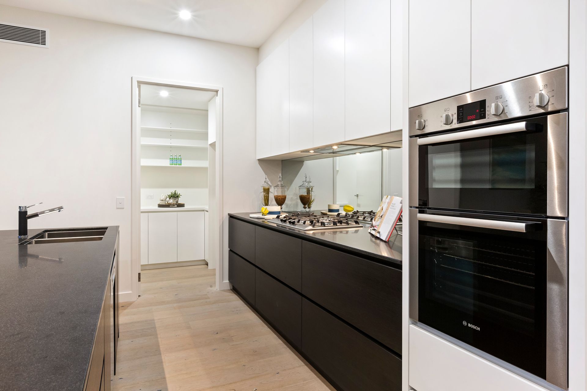 Modern white kitchen with dark cabinets, black countertop, and built-in oven — KM Custom Homes In Red Hill, VIC