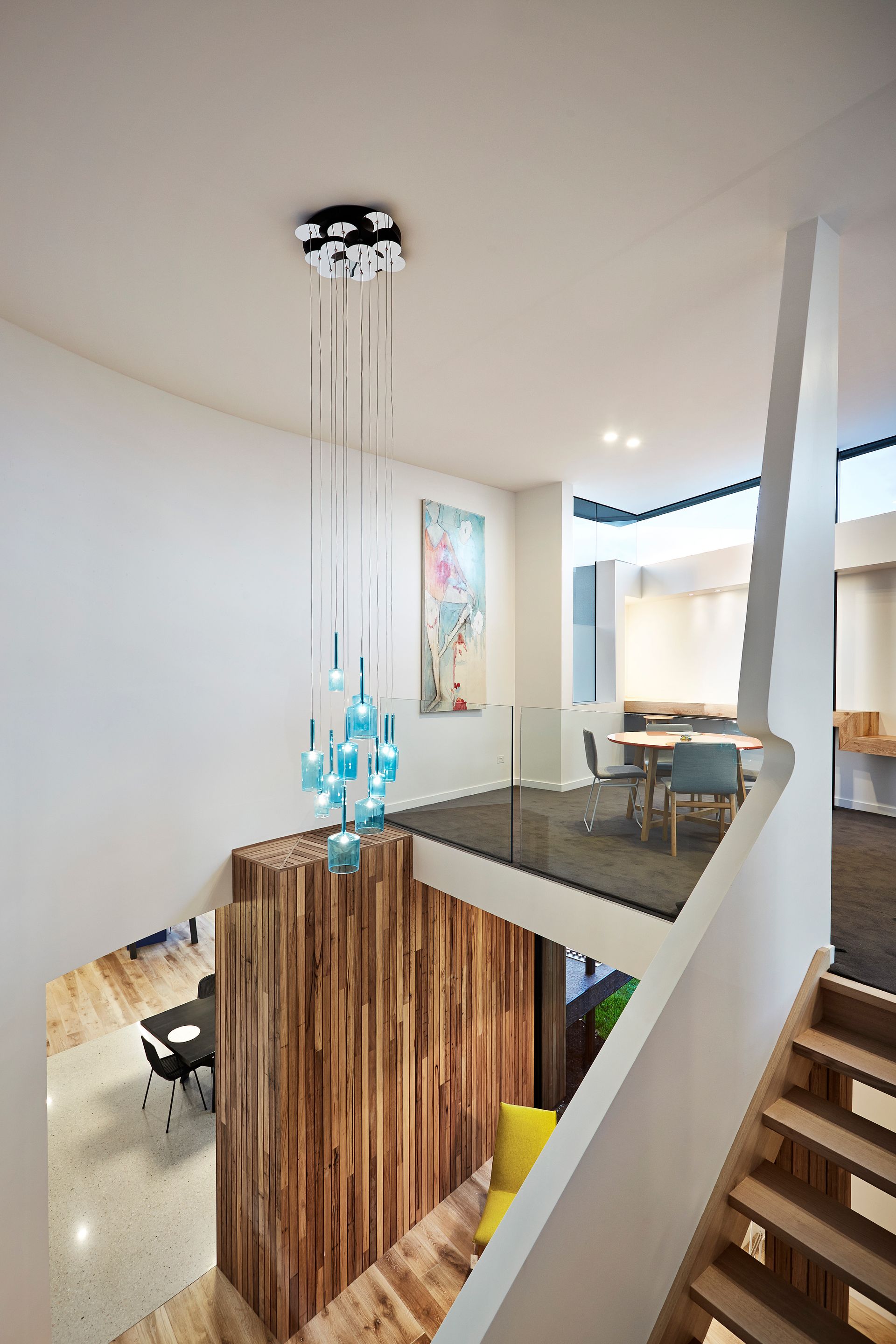 A Staircase In A House With A Glass Railing And A Chandelier Hanging From The Ceiling — KM Custom Homes In Mount Eliza, VIC
