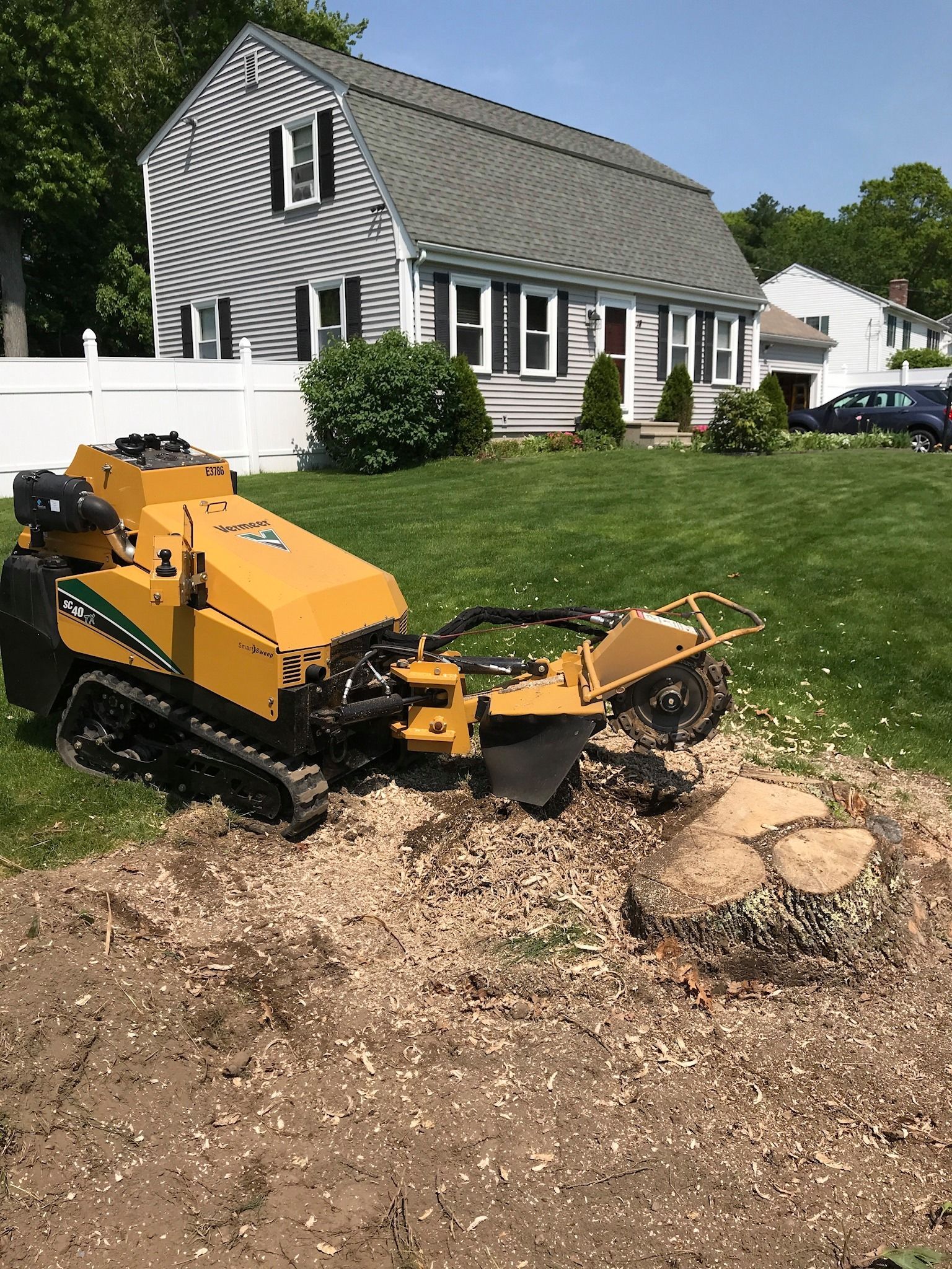 Yellow lawn mower mulching leaves beside a gray house and white fence
