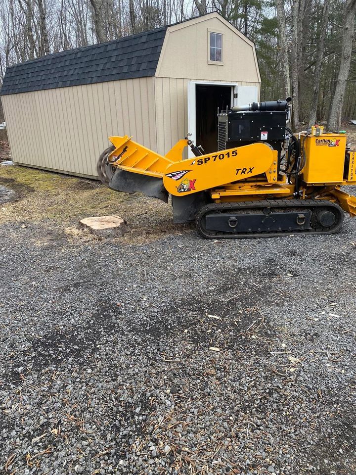 Yellow tracked loader beside an open shed door, dumping gravel on a driveway.