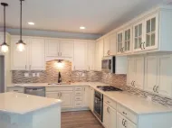 Bright white kitchen with cabinets, mosaic backsplash, granite counters, and pendant lights.