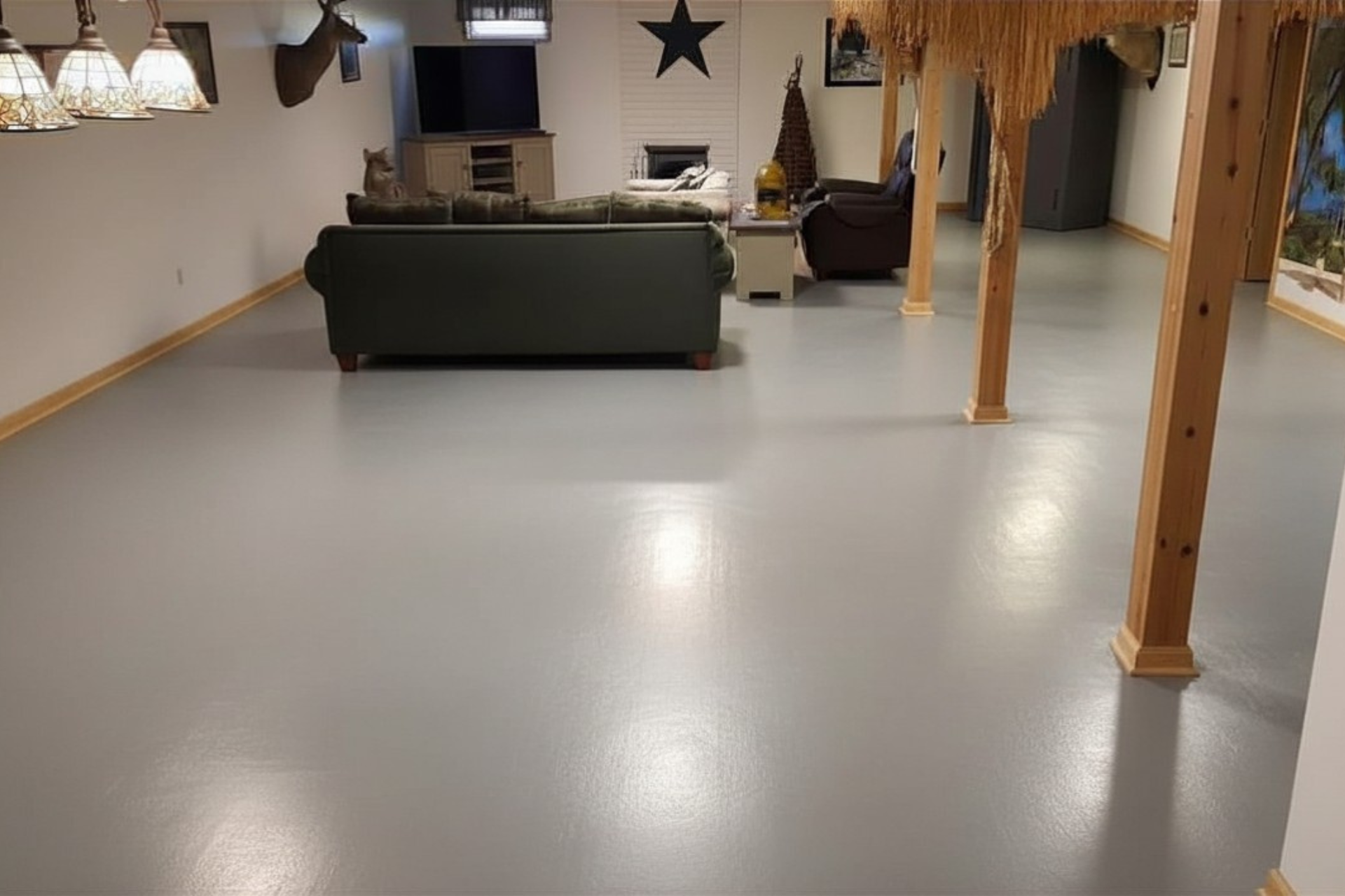 Empty basement room with gray floor, dark sofa, and wooden posts under hanging lights