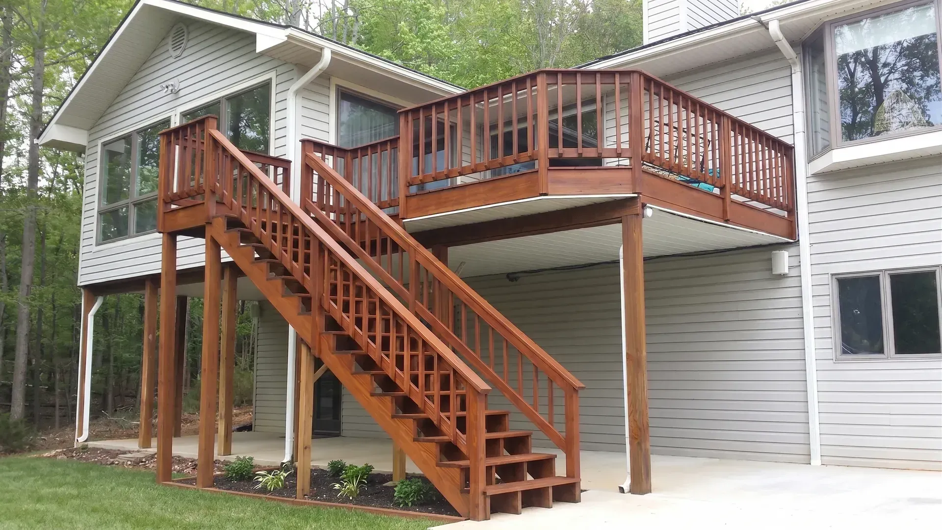 Wooden staircase and deck attached to a gray house on stilts in a wooded yard