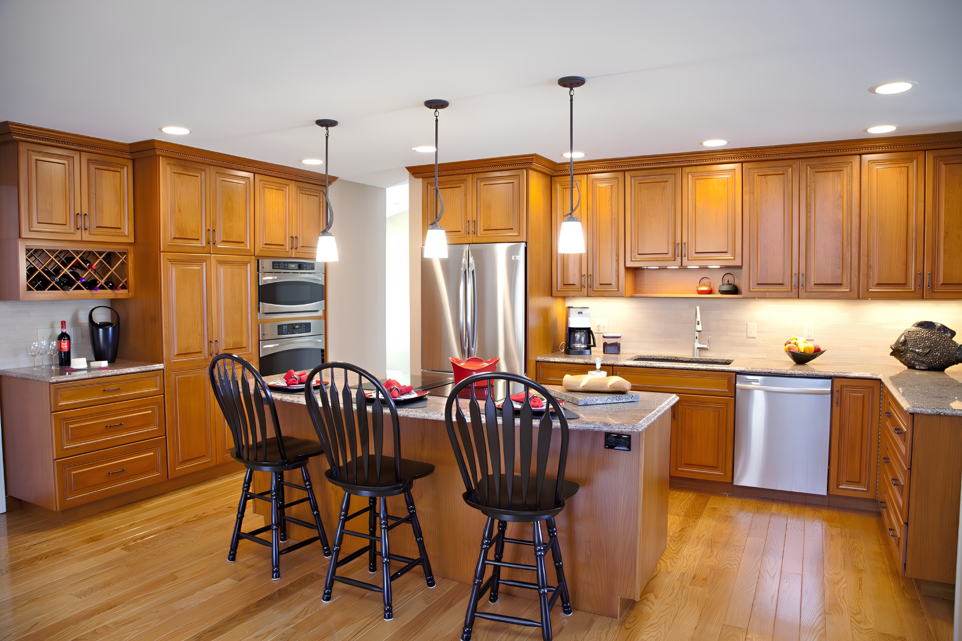 Spacious kitchen with wooden cabinets, island, and black bar stools under pendant lights.