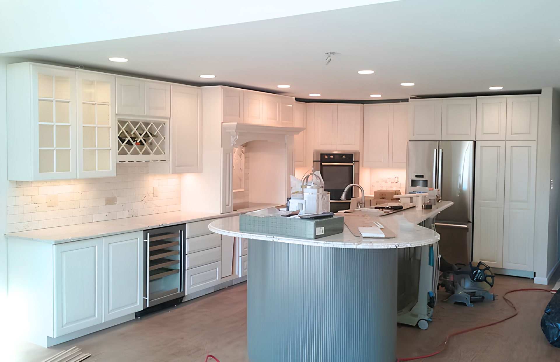 Bright modern kitchen with white cabinets, curved island, and two workers doing renovations
