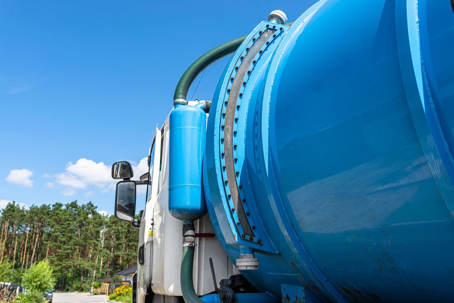 A blue vacuum truck is parked in front of a forest.