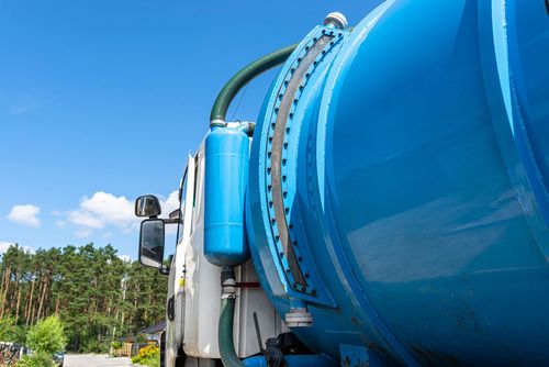 A blue vacuum truck is parked in front of a forest.