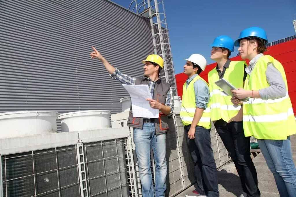 A group of construction workers are standing in front of a building looking at a blueprint.