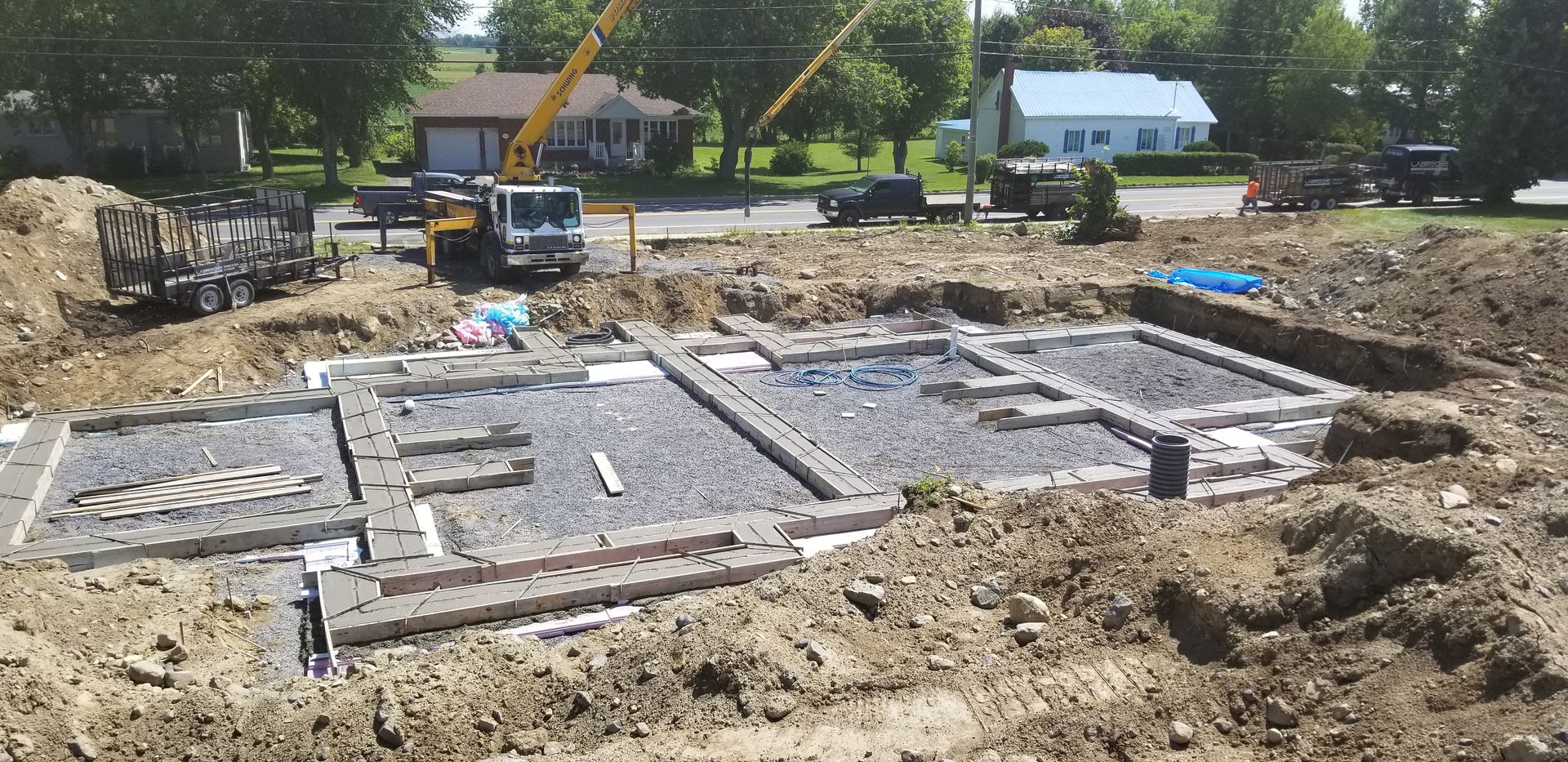 Chantier de construction avec coffrages de fondation en béton et une excavatrice en arrière-plan