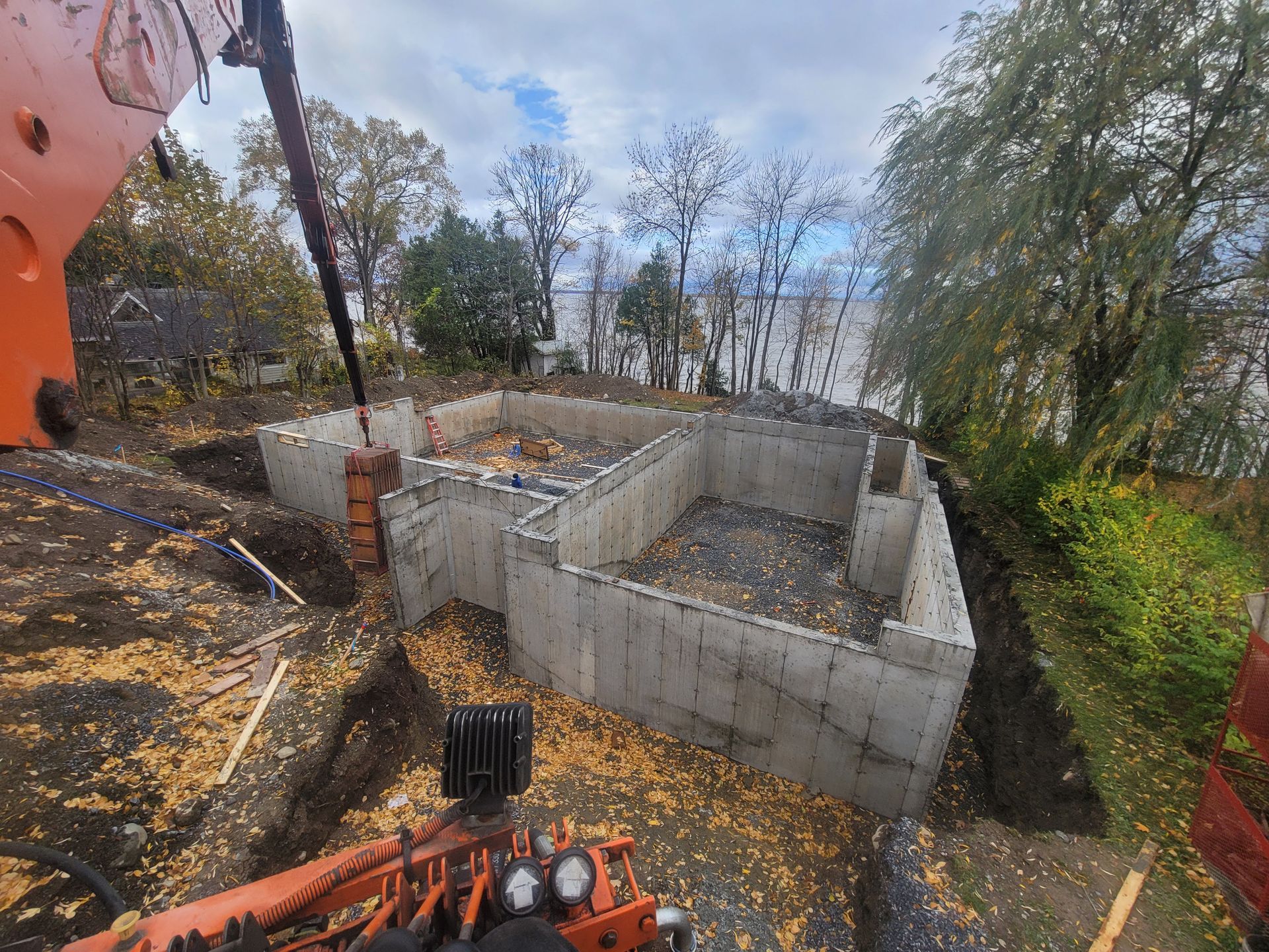 Fondations en parpaings partiellement construites sur un chantier boisé, vues depuis une excavatrice.