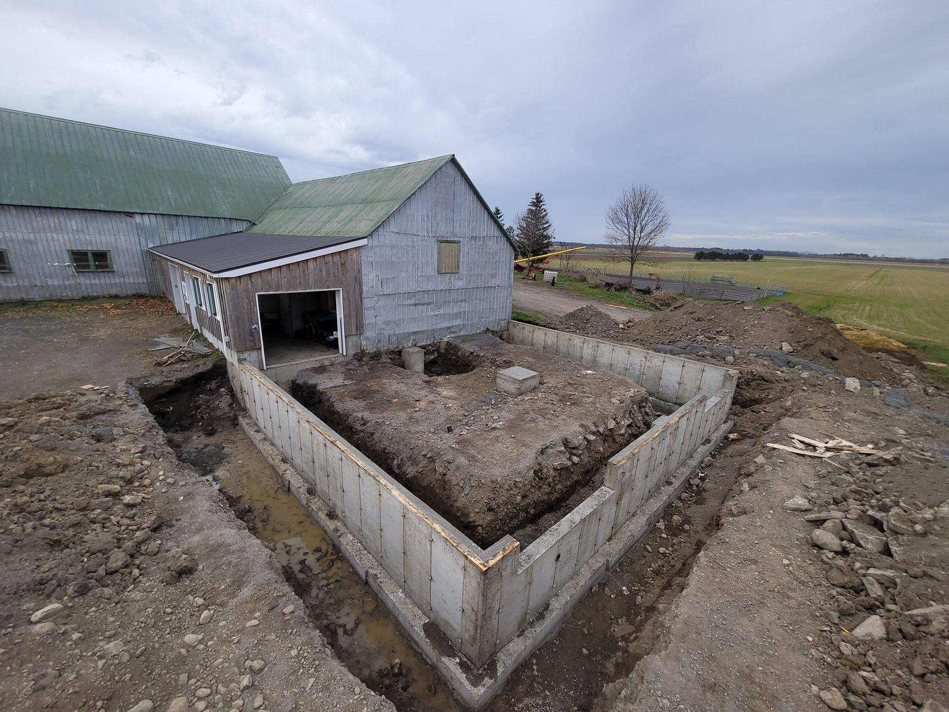 Cour de ferme rurale avec une grange, un enclos en béton et un espace boueux et vide sous un ciel couvert