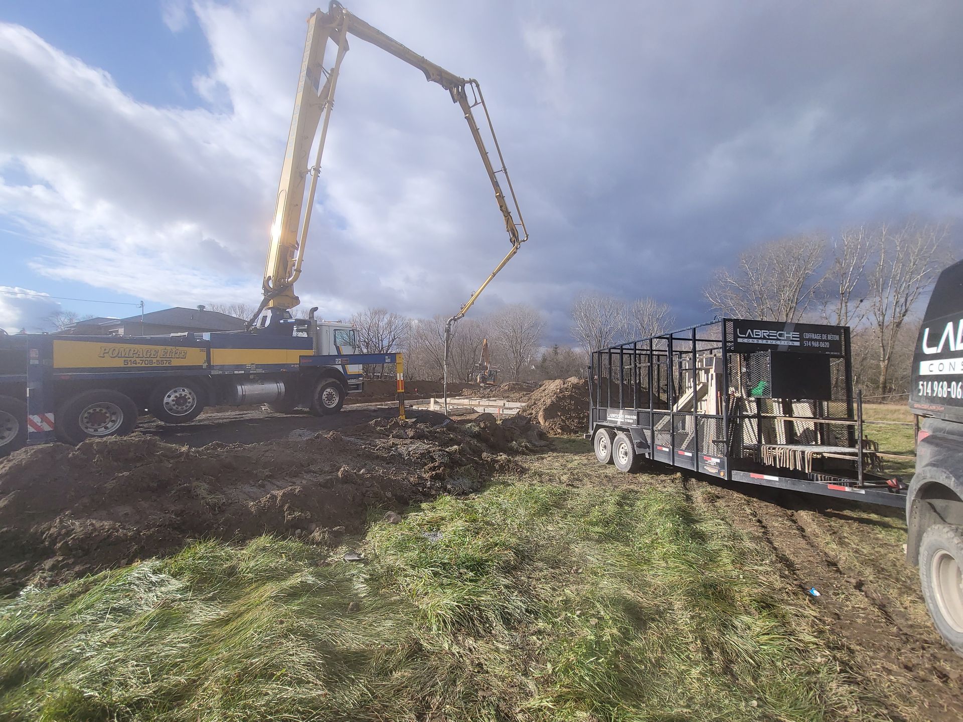 Déversement de béton par camion-pompe sur un chantier boueux sous un ciel nuageux