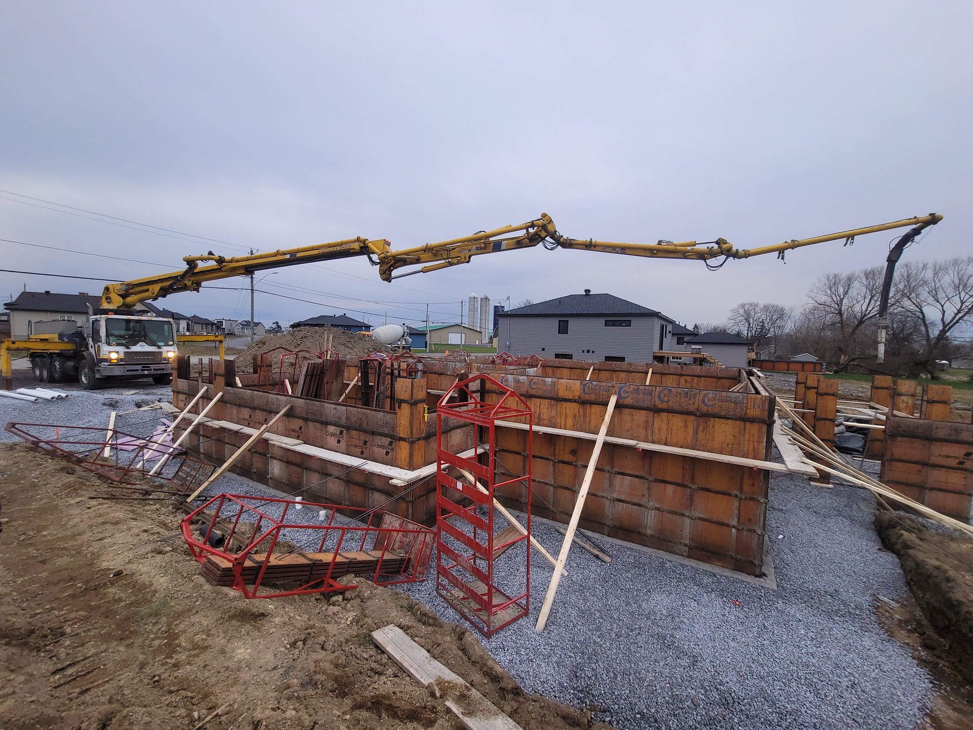 Pompe à béton coulant un mur de fondation sur un chantier de construction avec des ouvriers et du gravier sous un ciel couvert