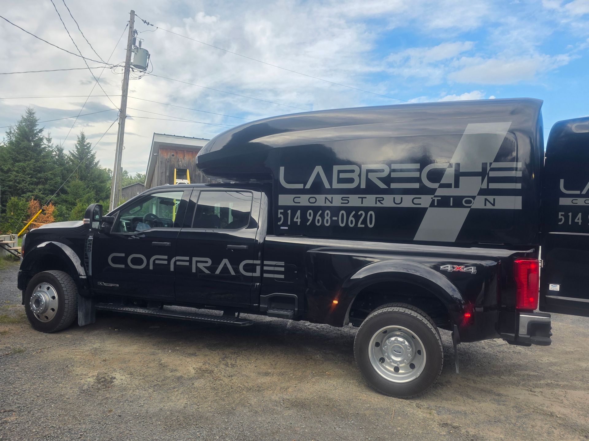 Camion de travail noir avec les inscriptions « LABRECHE » et « COFFRAGE » garé en bordure d'une route de gravier.