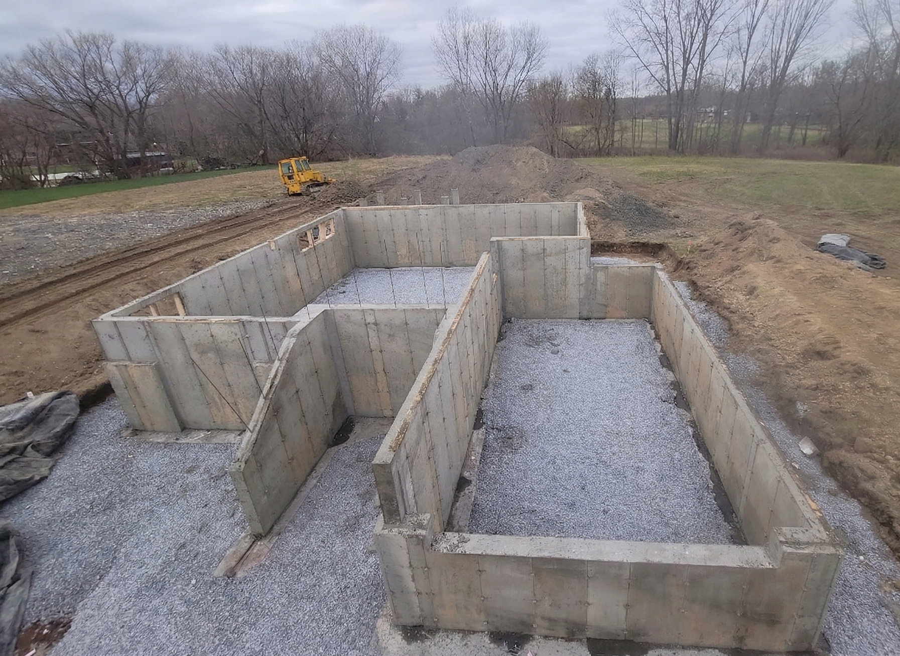 Coffrages de fondation en béton sur un chantier de construction en gravier, au bord d'une route boueuse