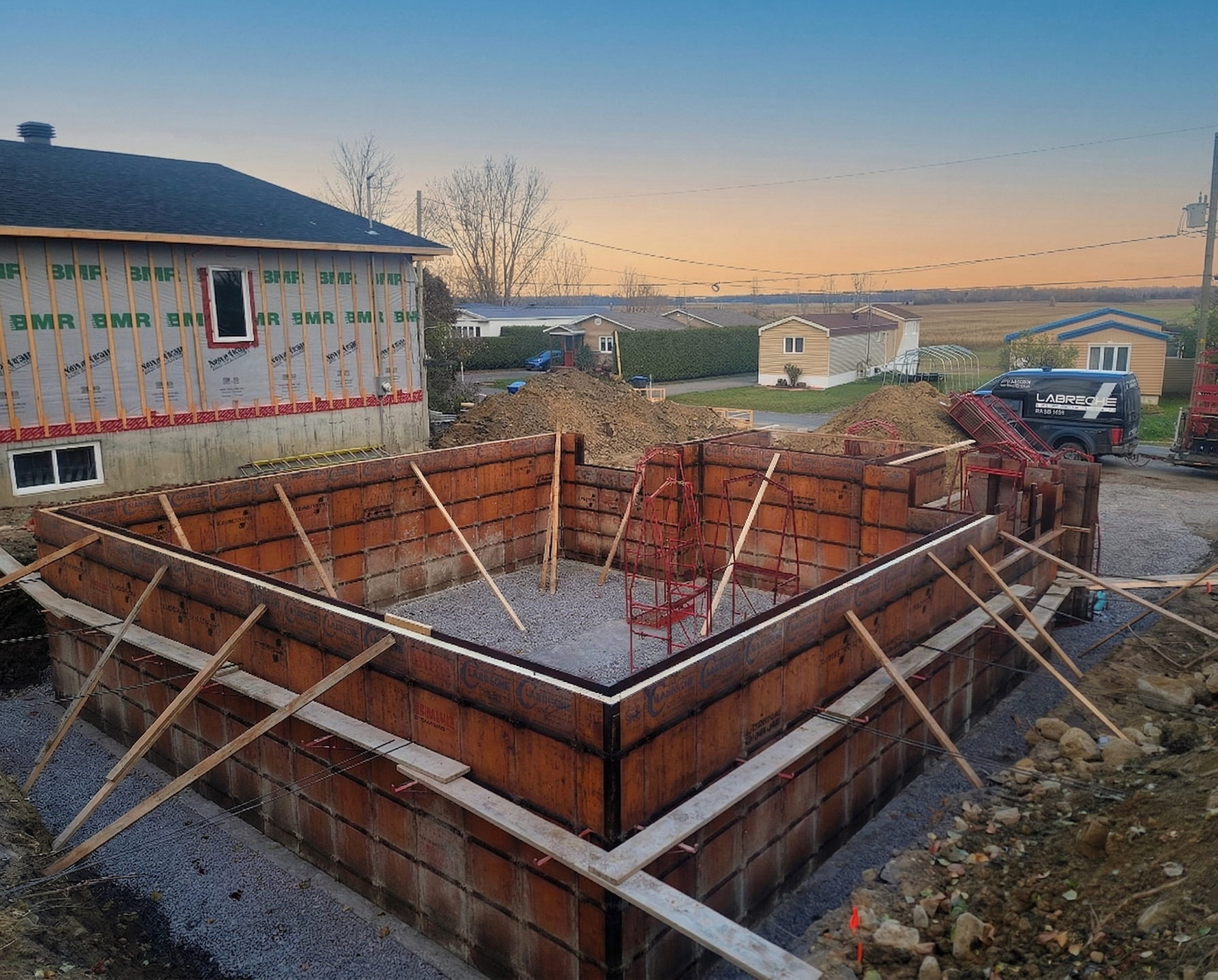 Fondation en briques en construction avec étaiement en bois sur un chantier en bord de route au crépuscule