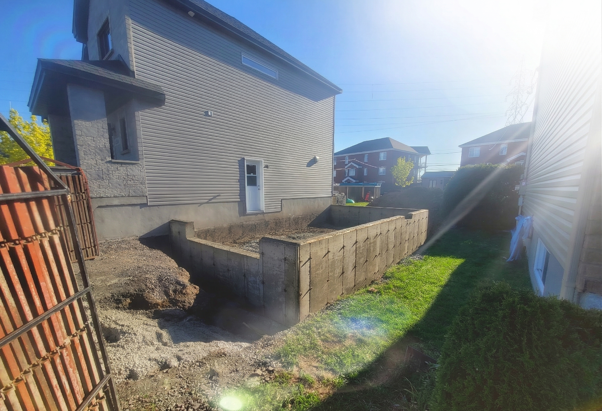 Cour arrière avec jardinière en béton, allée en gazon et soleil à côté d'une maison au bardage ondulé.