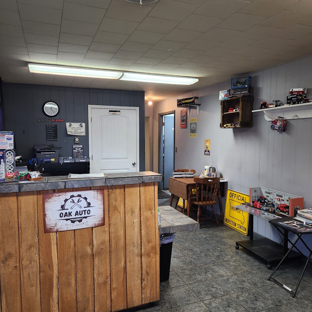 Small lobby shop interior with a wooden counter, gray walls, shelves, and model cars on display. | Oak Auto