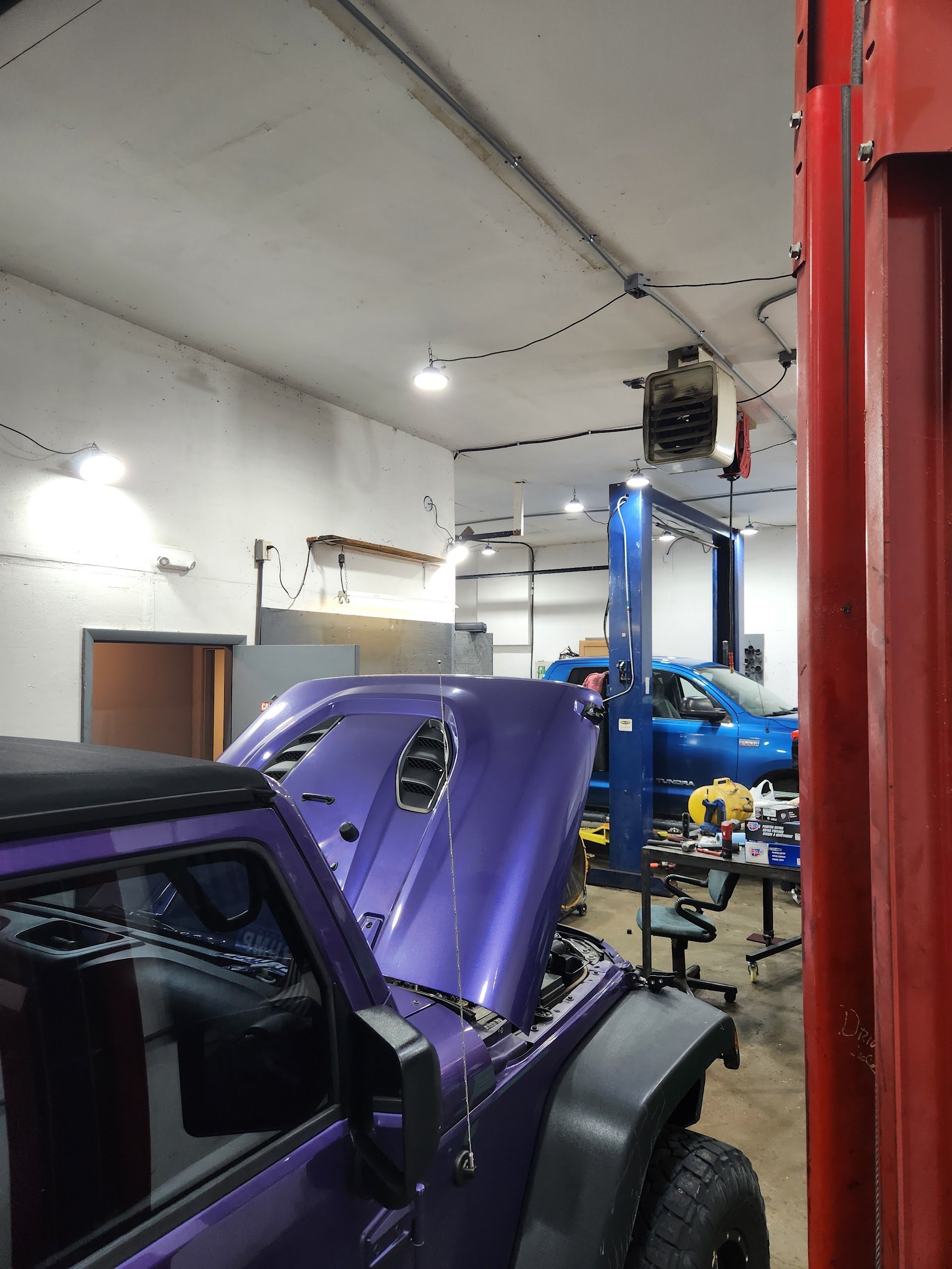 Purple classic car in an auto shop with its hood open on a lift, surrounded by tools and equipment | Oak Auto