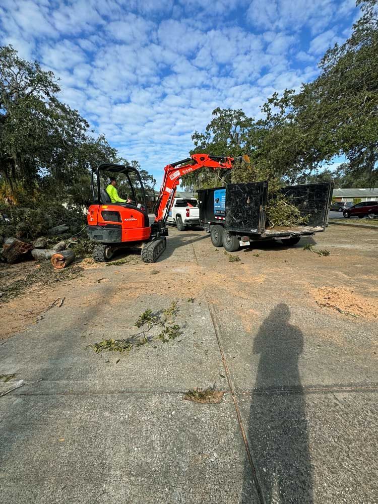 A man is driving a small excavator in a parking lot.