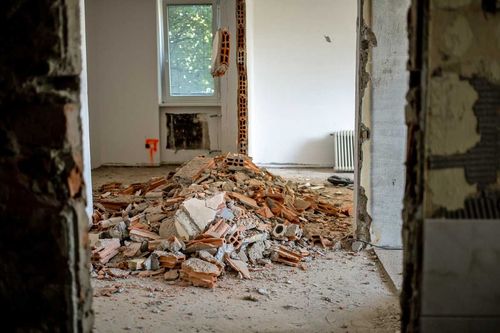 Room under renovation, showing debris pile of brick and plaster. View through a doorway.