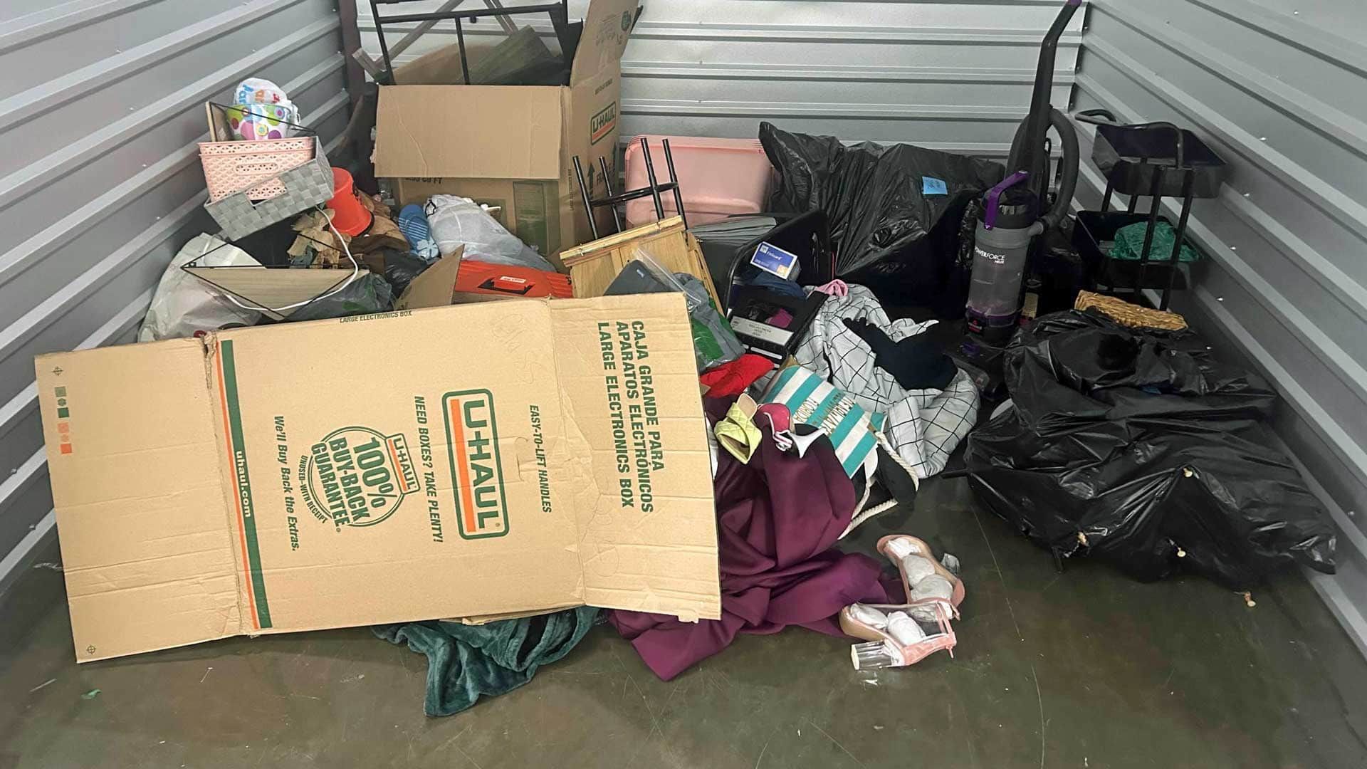Storage unit, cluttered with boxes, clothing, and miscellaneous items.