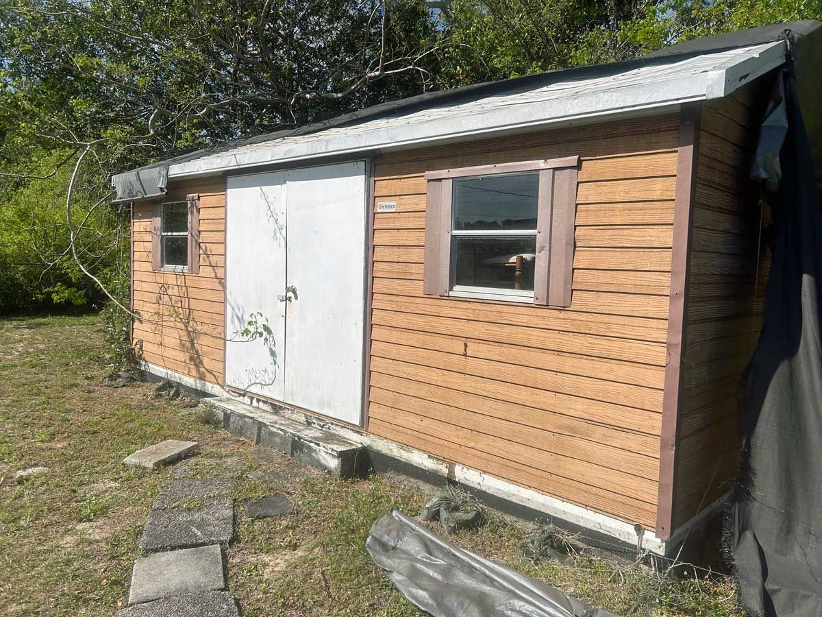 A small wooden shed with a white door and windows is sitting in the middle of a grassy field.