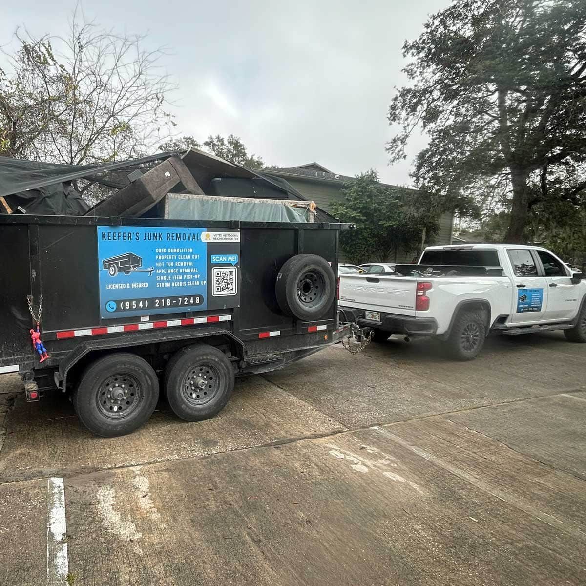 A dumpster is being towed by a Keefer's truck in a parking lot.