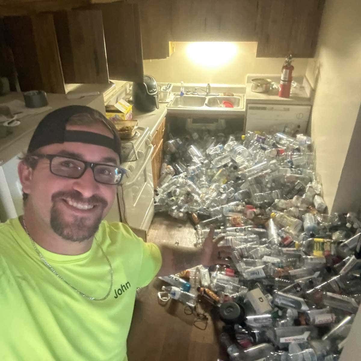 John Keefer in a yellow shirt standing in a messy kitchen