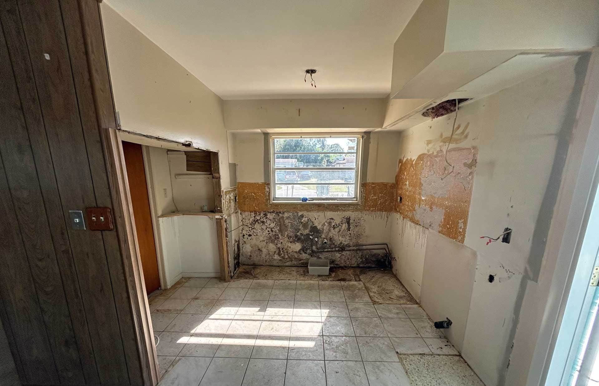 Empty kitchen renovation in progress; damaged walls, exposed drywall, and debris.