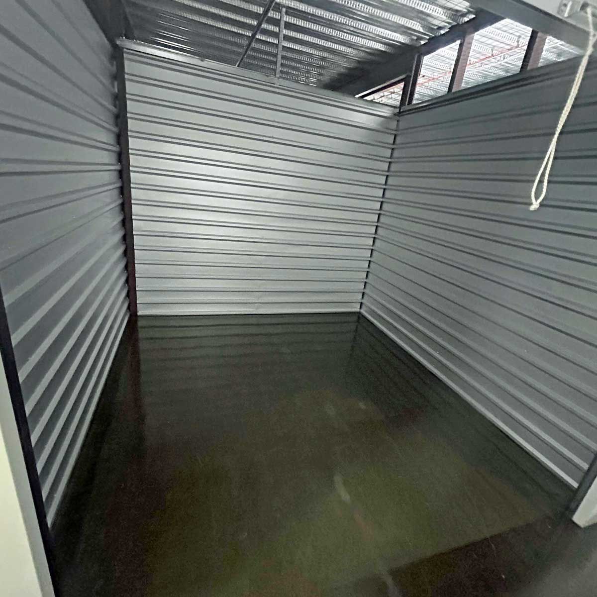 An empty storage unit with a gray wall and a black floor.