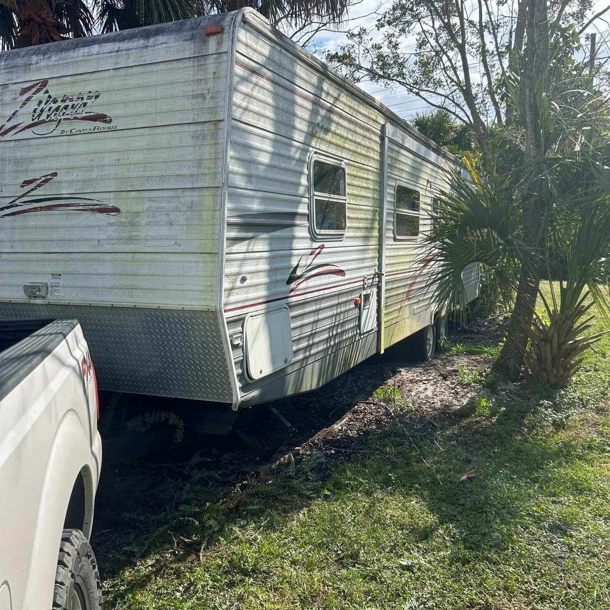 A trailer is parked in the grass next to a truck.