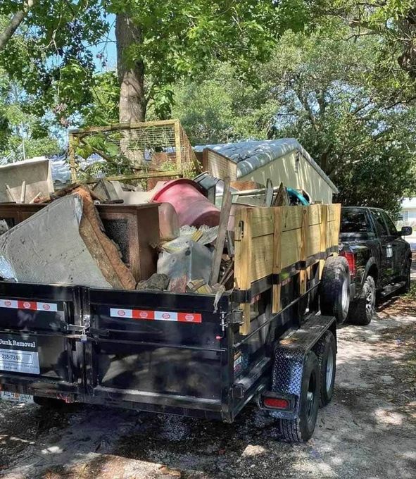 A dumpster trailer filled with junk is parked in a driveway next to a truck.