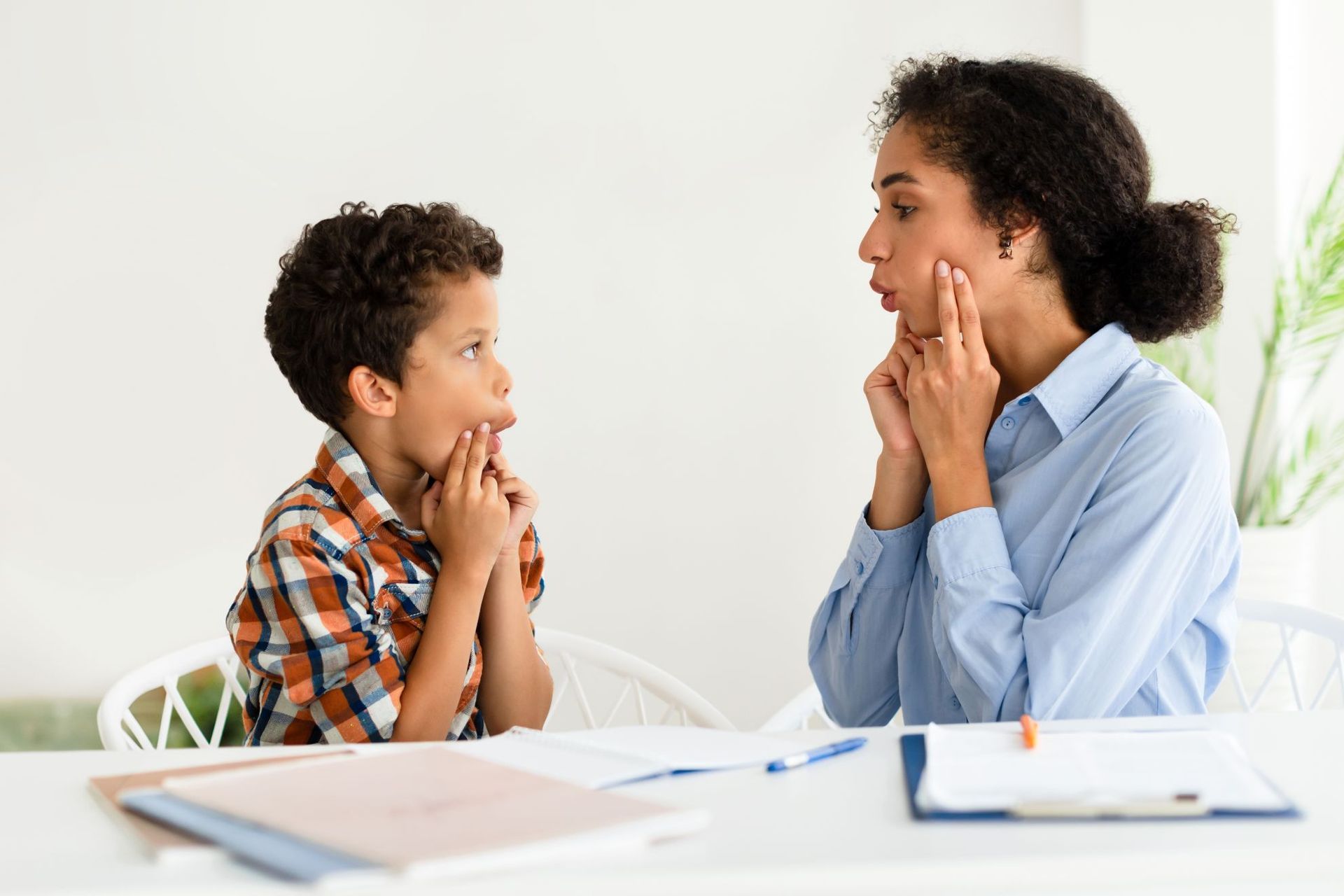 Boy and woman practicing speech sounds, both touching their cheeks.