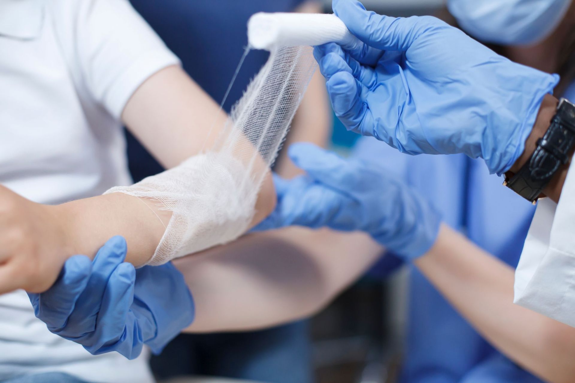 Person's arm being bandaged by someone wearing blue gloves; indoors.