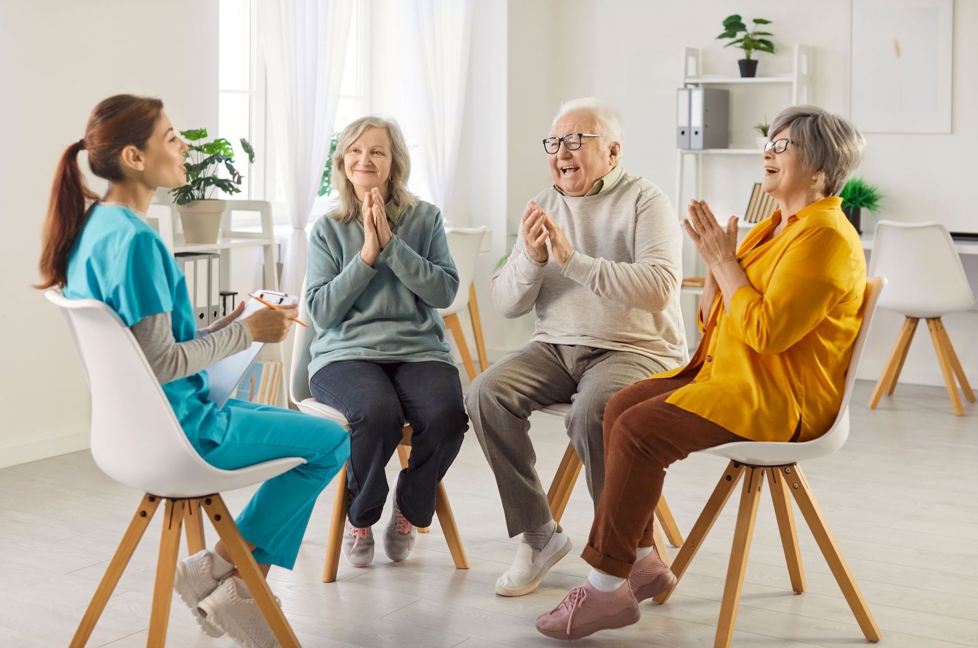 A nurse leads a group of seniors in a circle, all clapping in an indoor setting.