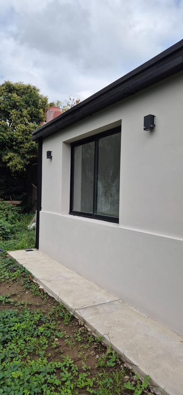 Pared exterior de una casa moderna con una gran ventana, revestimiento gris claro y un camino de hormigón junto al césped.