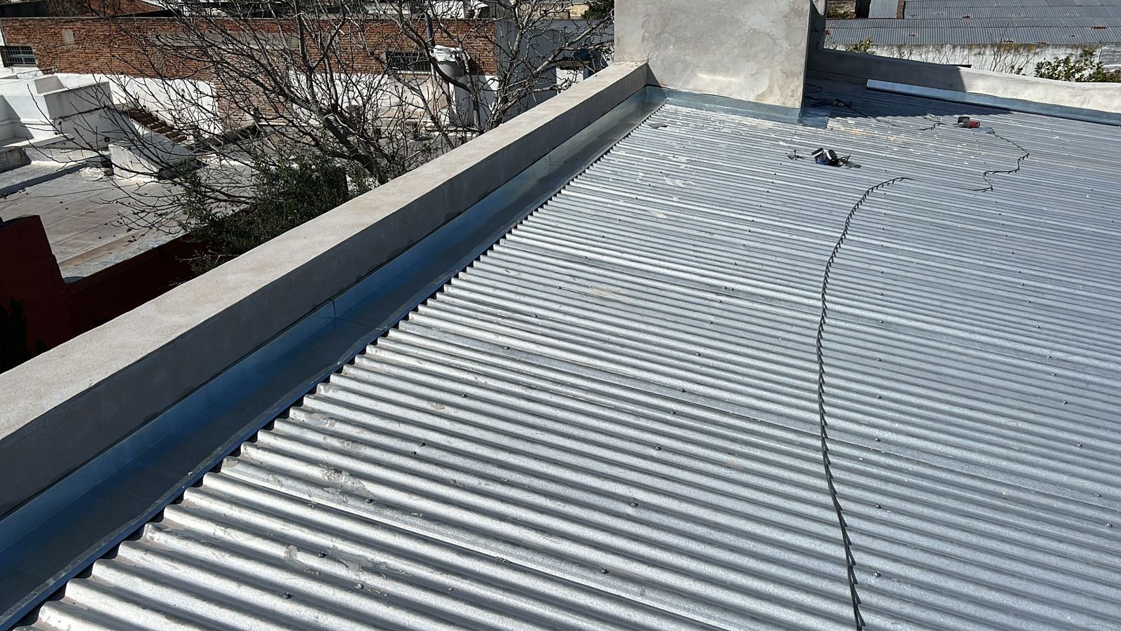 Techo de chapa ondulada con un largo cable que lo atraviesa, visto desde arriba en un día soleado.