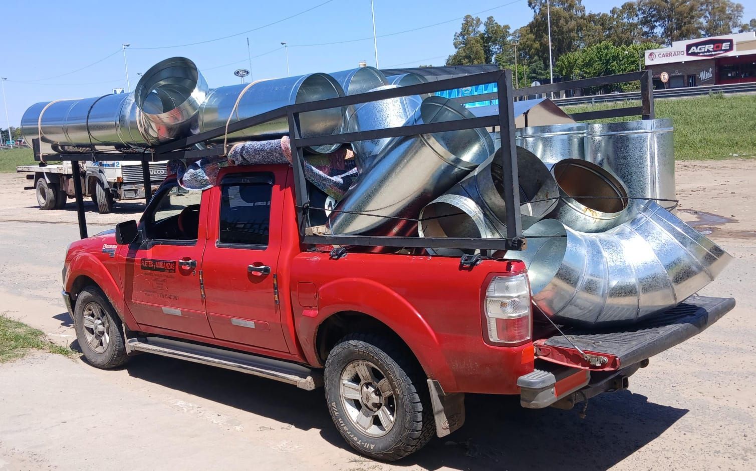 Una camioneta roja cargada de tuberías y conductos de metal brillante estaba estacionada al aire libre en una zona soleada.