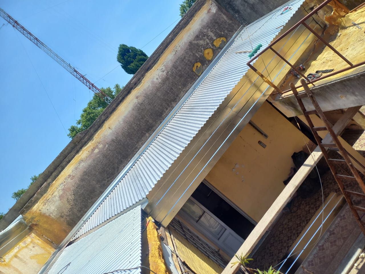 Vista inclinada de un edificio amarillo con techo de metal y cielo azul, que muestra un porche y un balcón.