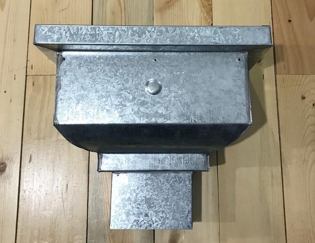 Caja de metal galvanizado con brida superior, apoyada sobre un suelo de madera.