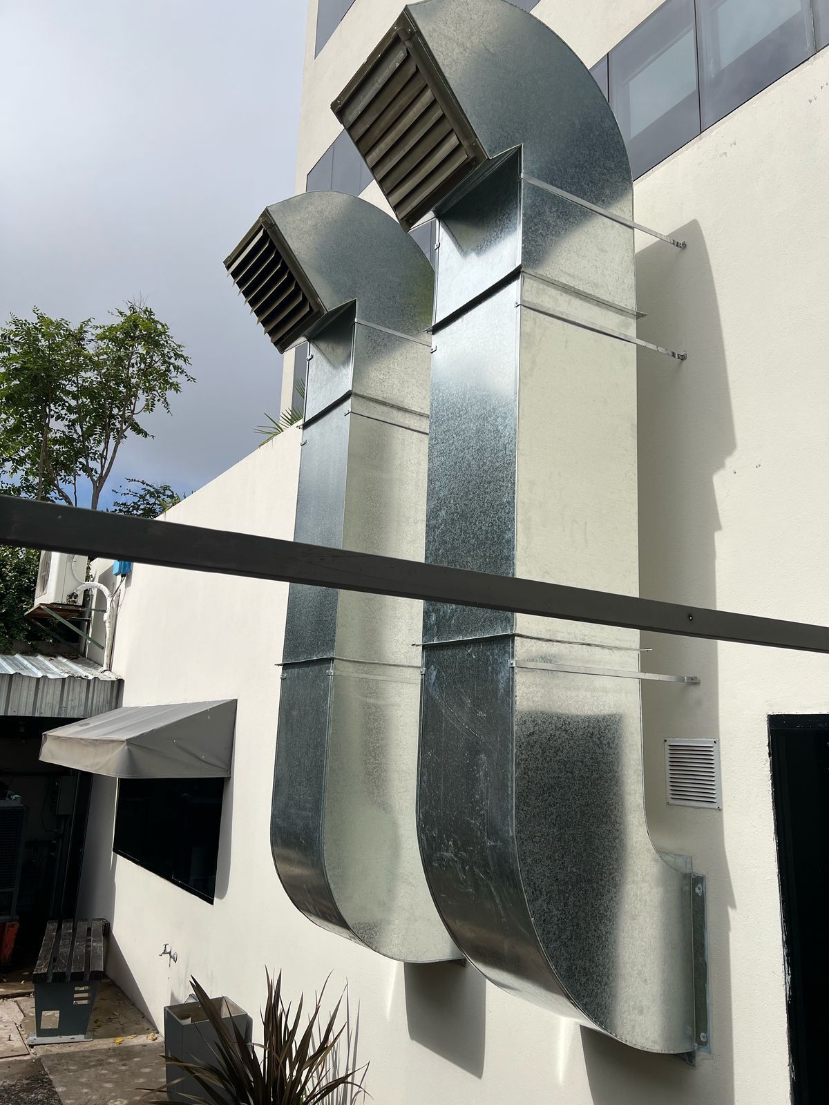 Grandes conductos de ventilación metálicos instalados en la fachada blanca de un edificio bajo un cielo nublado.