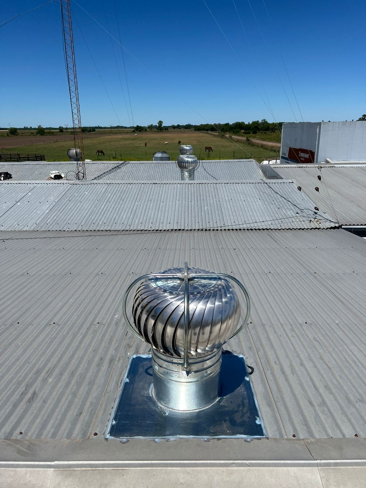Ventilador de turbina de techo metálico en un tejado gris bajo un cielo azul claro.
