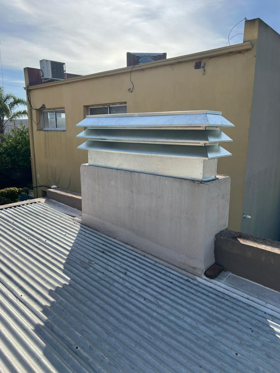 Chimenea de ventilación en la azotea con lamas metálicas en un tejado plano junto a un edificio de color beige.