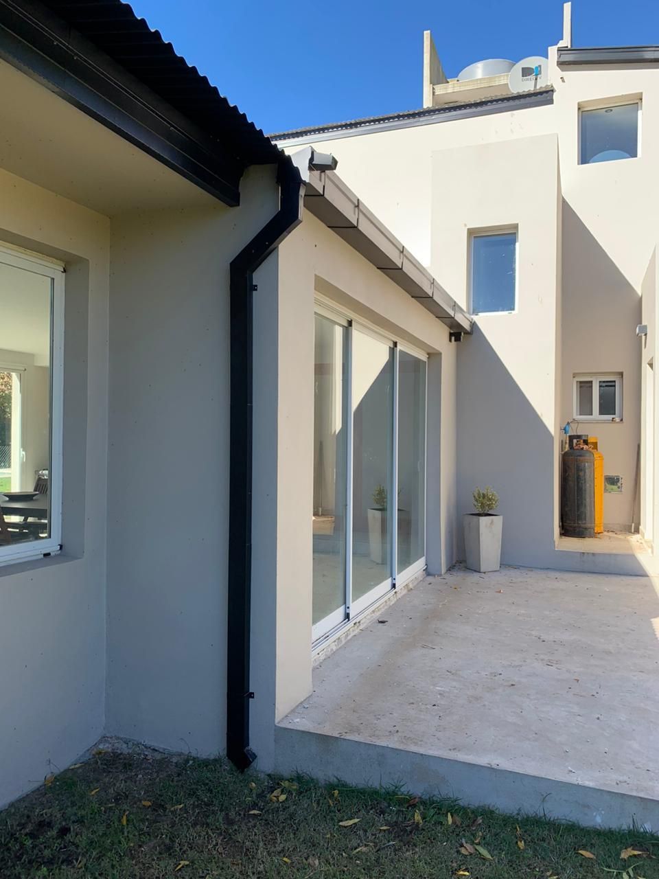 Patio exterior junto a una casa blanca con puertas corredizas de vidrio y una pequeña planta en maceta.