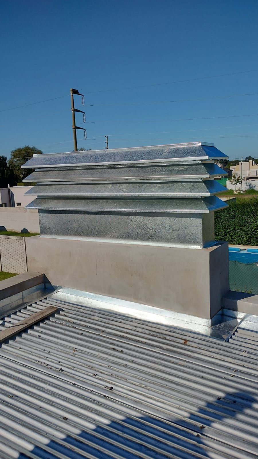 Ventilador de techo con rejillas metálicas y base blanca bajo un cielo azul despejado.