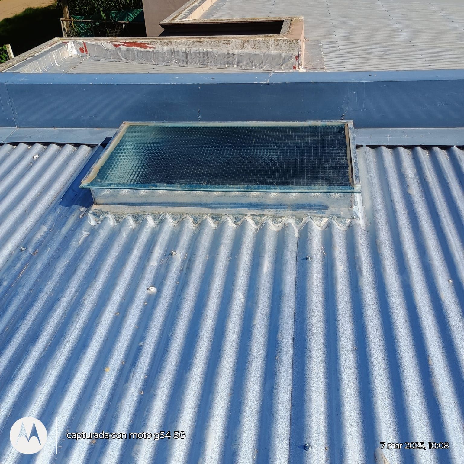 Techo de chapa ondulada azul con tragaluz rectangular y ventilación en el techo, bañado por la luz del sol.