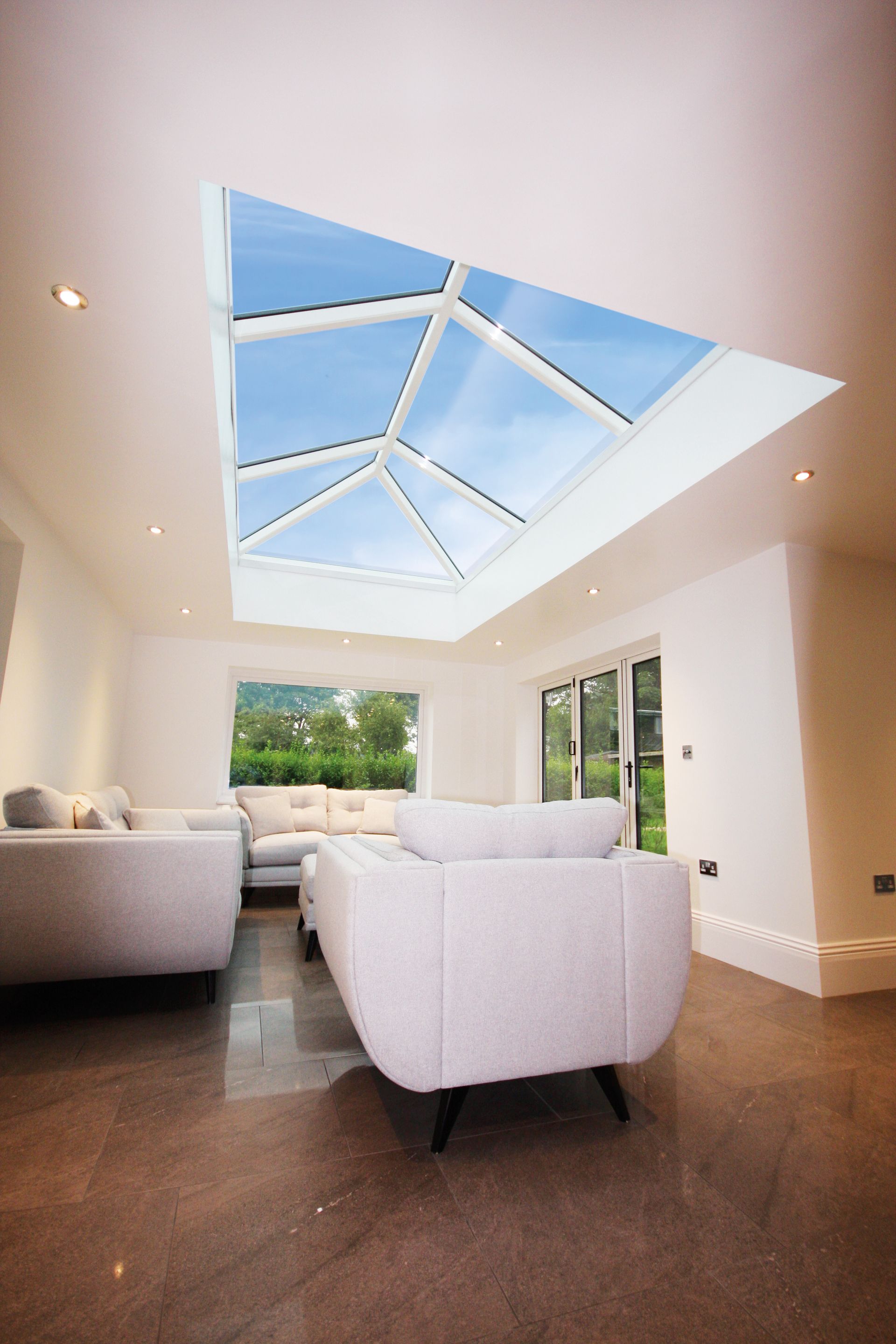 Bright, modern living room with large skylight, white walls, gray furniture, and brown floors.