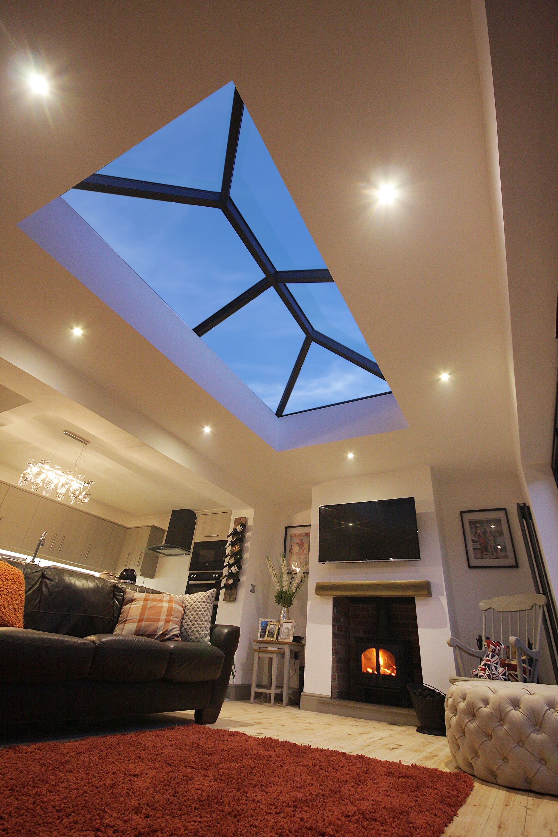 Modern living room with a large skylight, fireplace, sofa, and red rug.