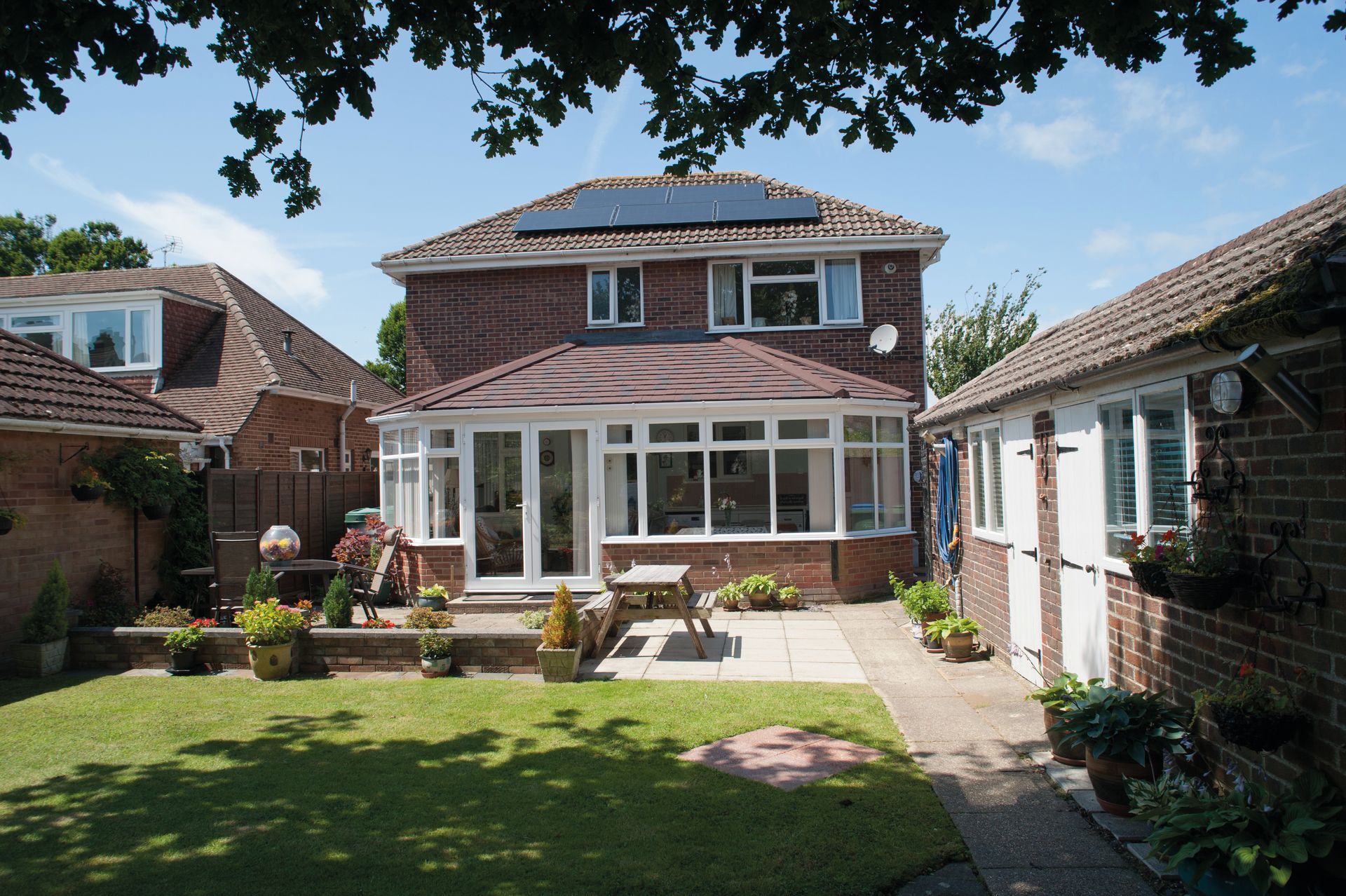 Backyard of a brick house with a sunroom, patio, and green lawn on a sunny day.